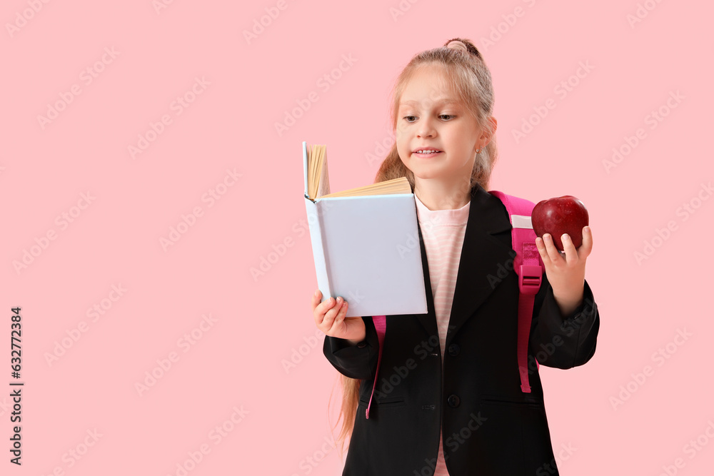 Little schoolgirl with book and apple on pink background