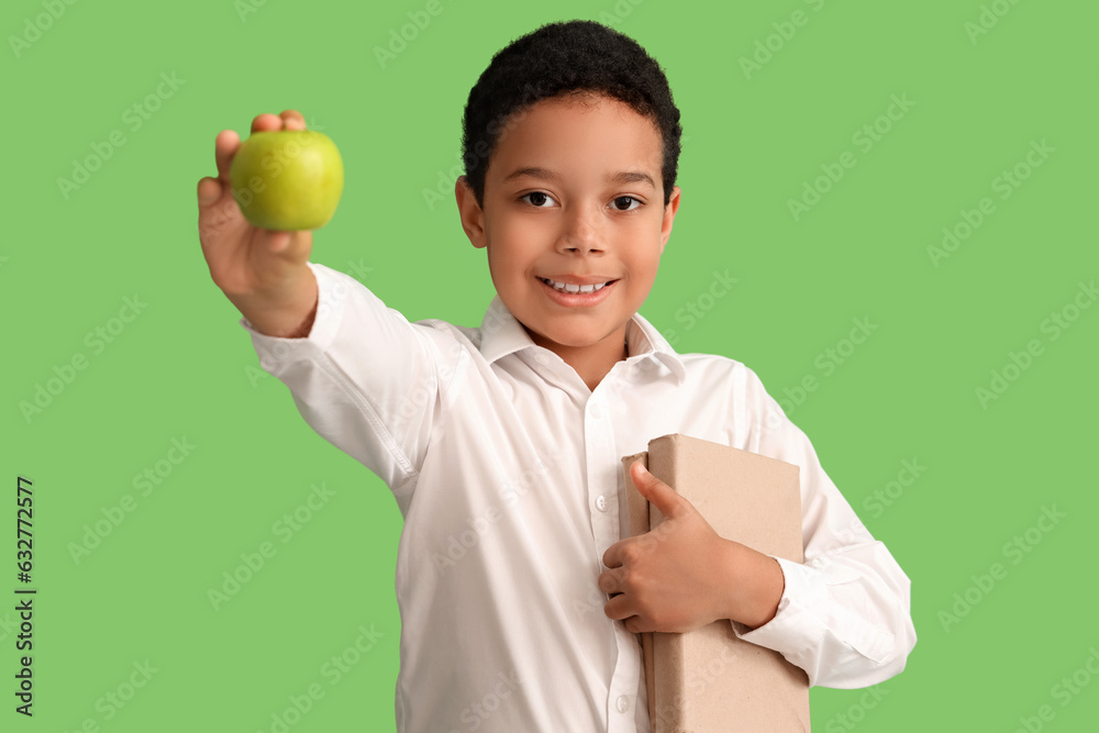 Little African-American schoolboy with books and apple on green background