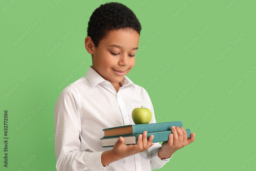 Little African-American schoolboy with books and apple on green background