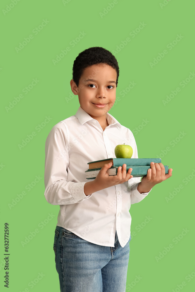 Little African-American schoolboy with books and apple on green background