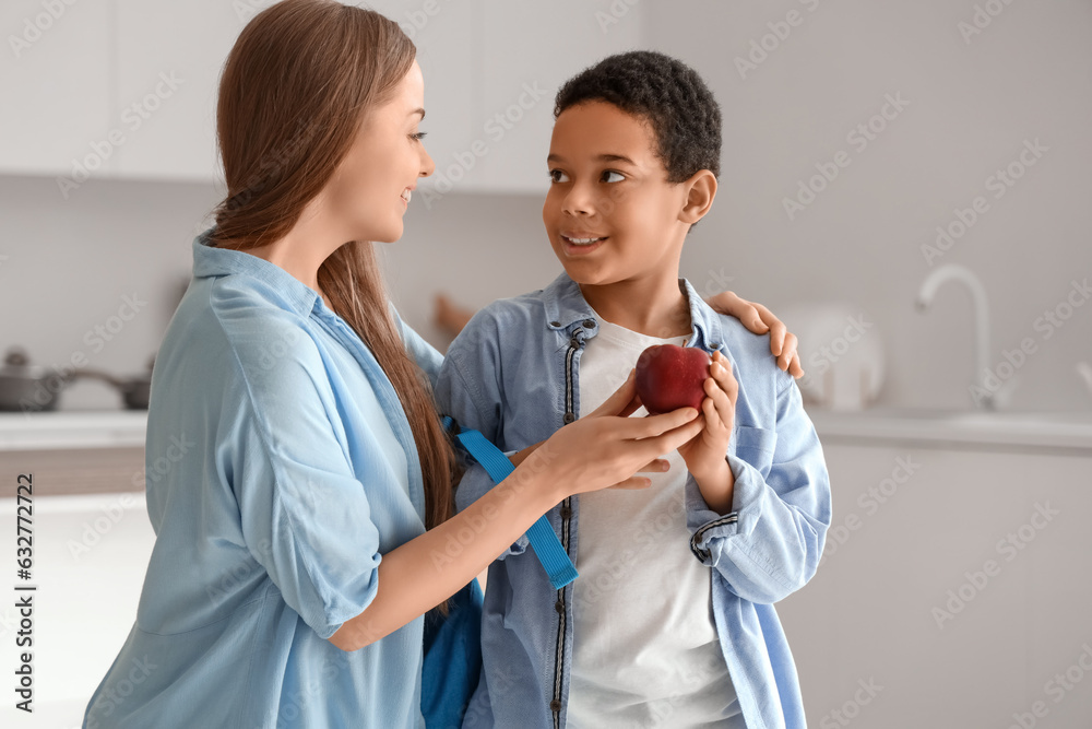 Mother giving apple to little schoolboy in kitchen