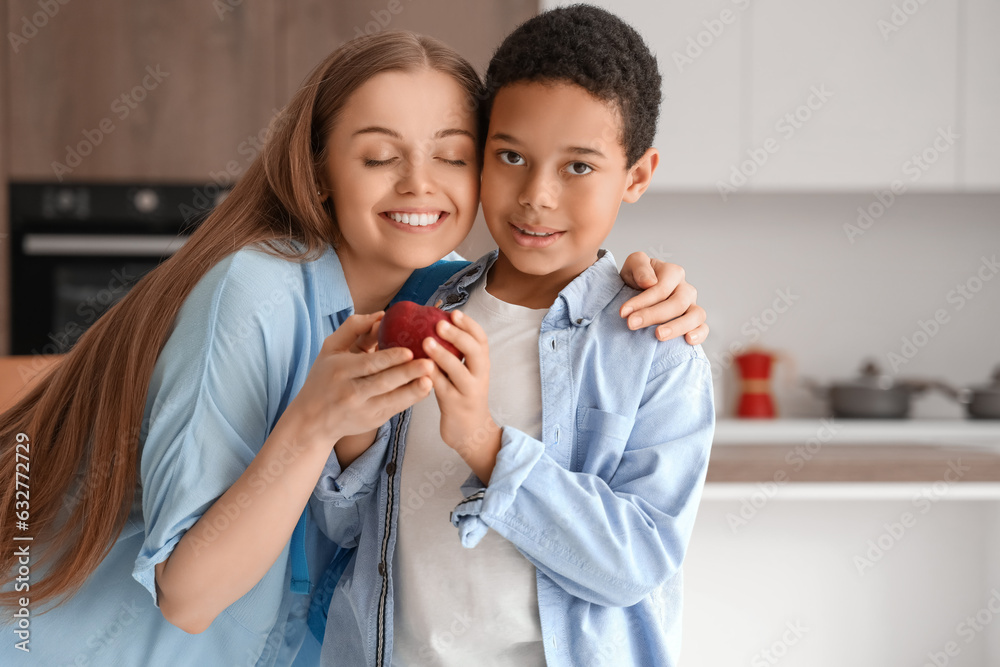 Mother giving apple to little schoolboy in kitchen