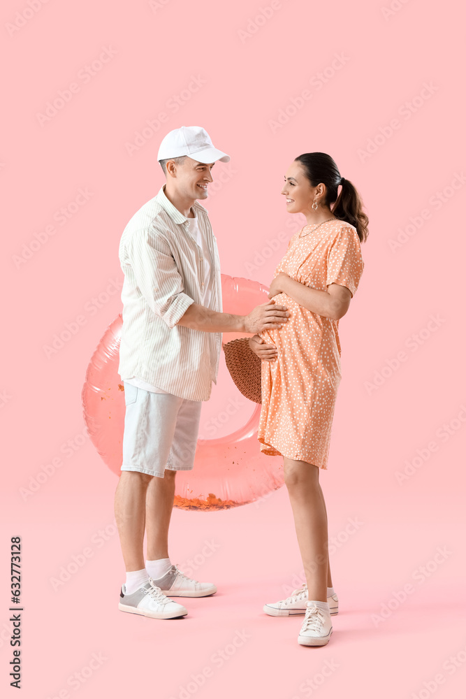 Young pregnant couple with inflatable ring on pink background