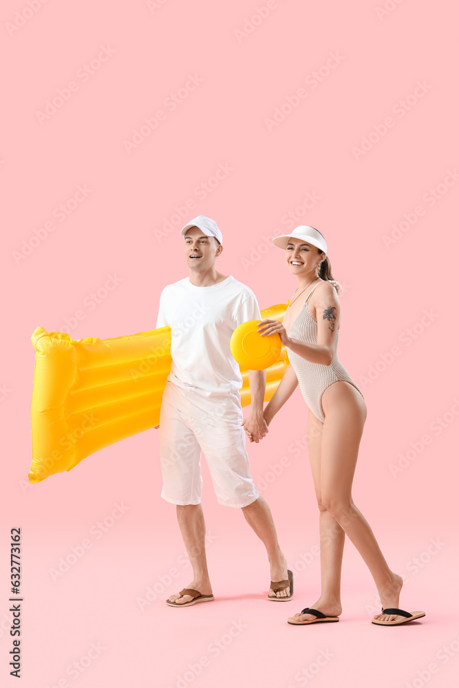 Young couple with inflatable mattress and frisbee walking on pink background