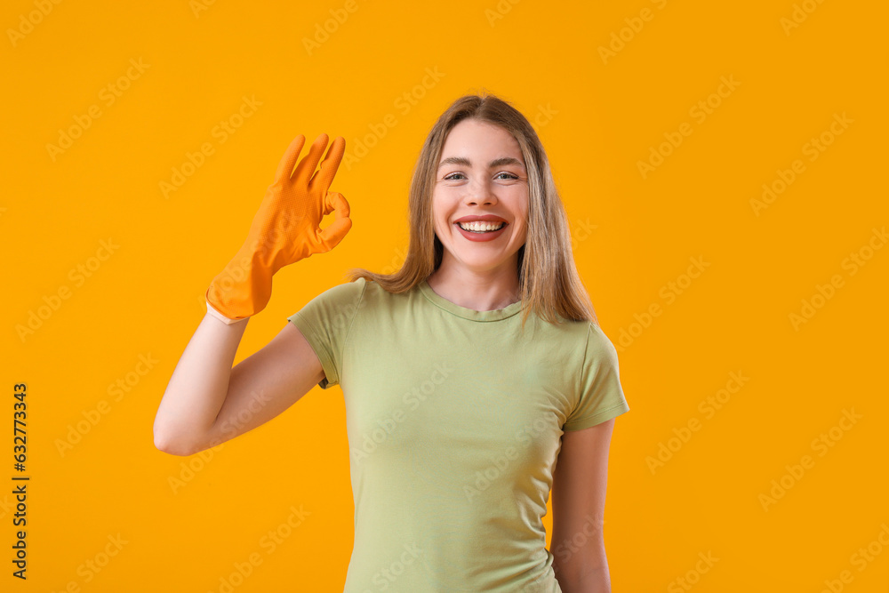 Young woman in rubber glove showing OK on orange background