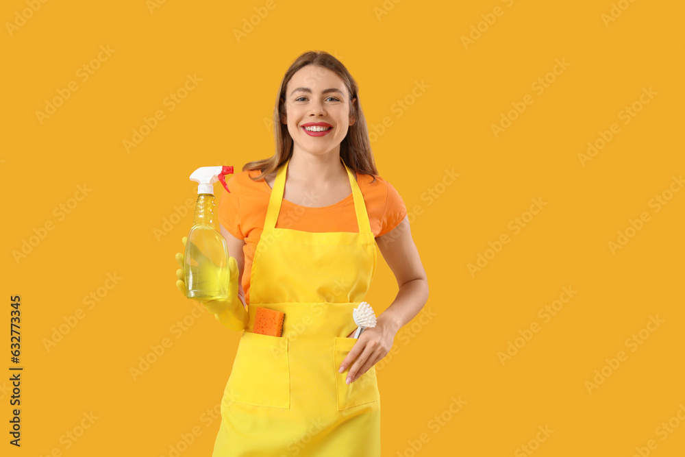 Young woman with bottle of detergent and cleaning brush on orange background