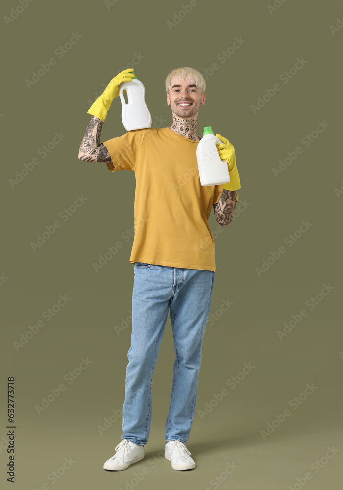 Young tattooed man with bottles of detergent on green background