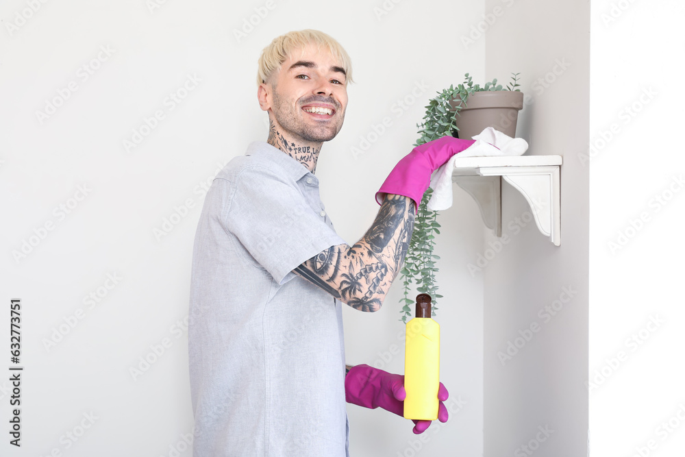 Young tattooed man cleaning shelf at home