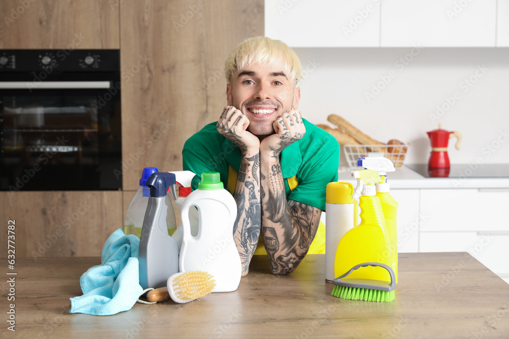 Young tattooed man with cleaning supplies at table in kitchen