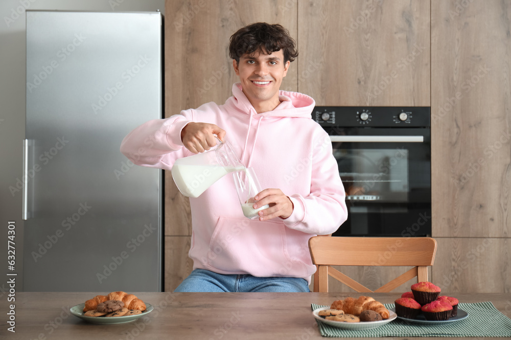 Young man pouring milk into glass  in kitchen