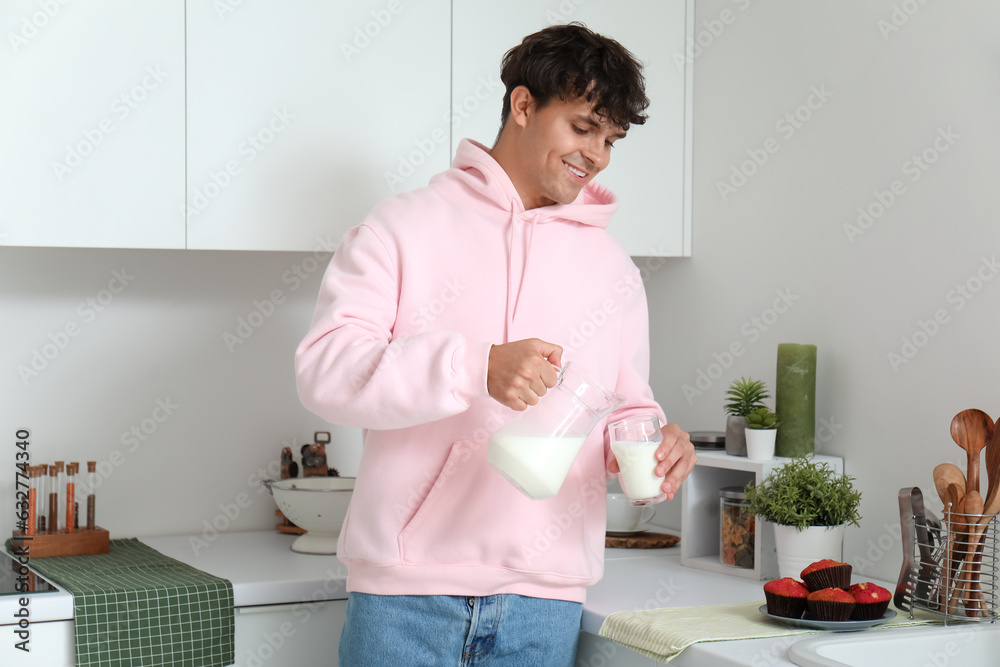 Young man pouring milk into glass  in kitchen