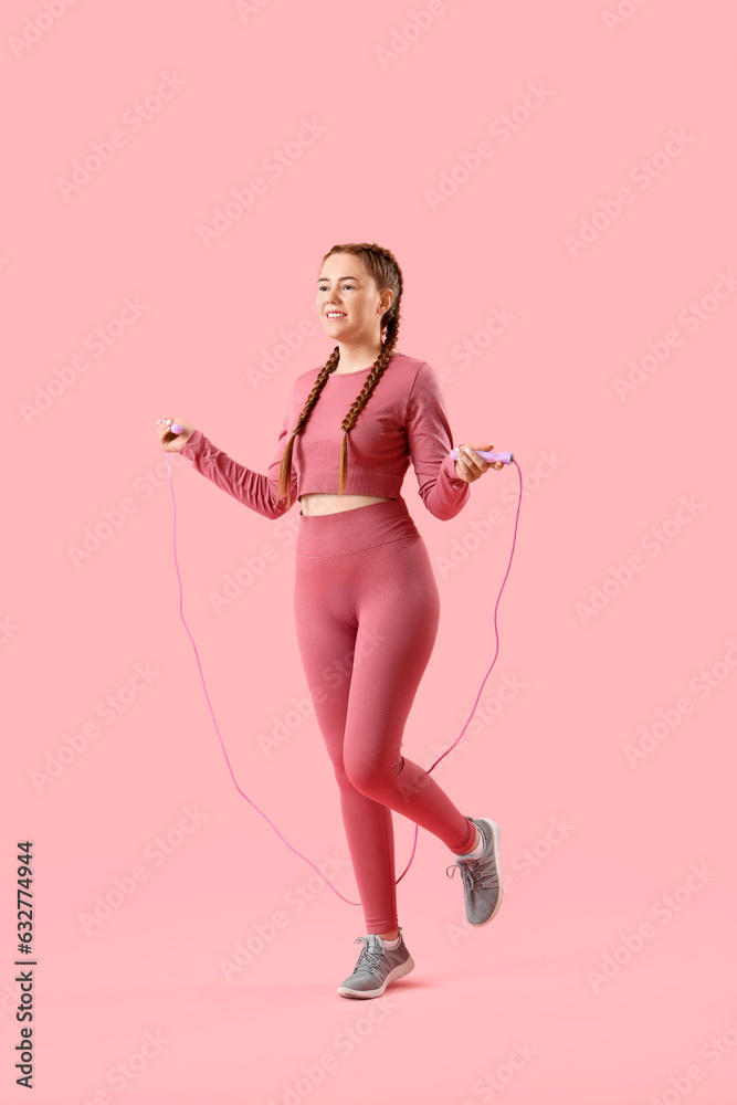 Sporty young woman jumping with rope on pink background