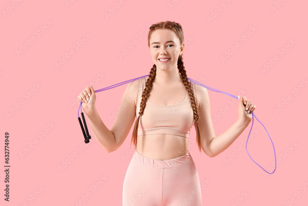 Sporty young woman with skipping rope on pink background