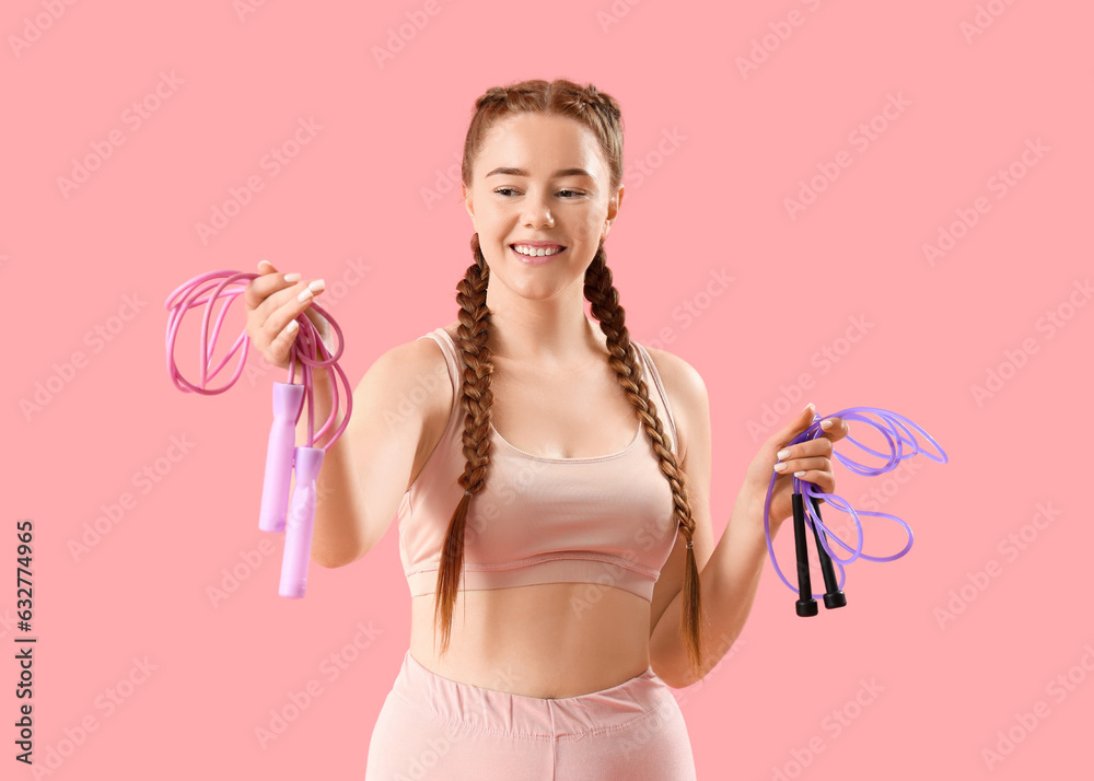 Sporty young woman with ropes on pink background