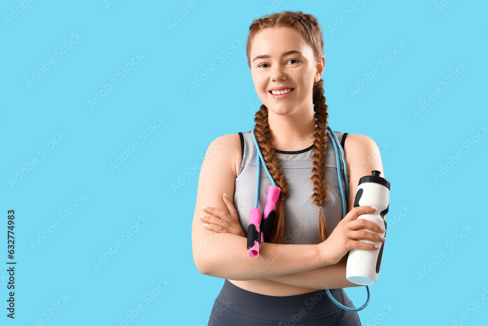 Sporty young woman with skipping rope and bottle of water on blue background