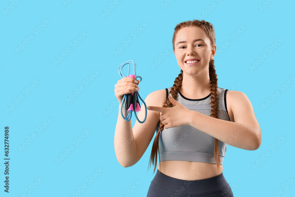 Sporty young woman pointing at skipping rope on blue background