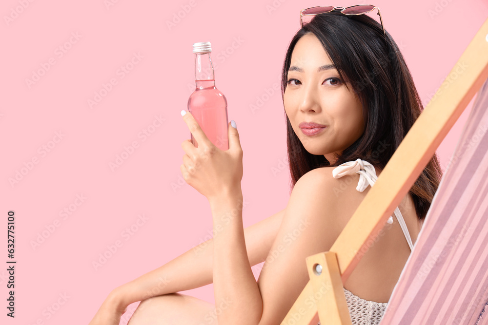 Beautiful Asian woman with soda relaxing in deck chair on pink background, closeup