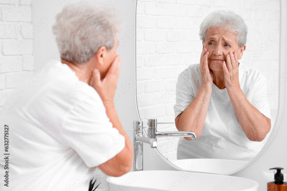 Upset senior woman looking in mirror at home