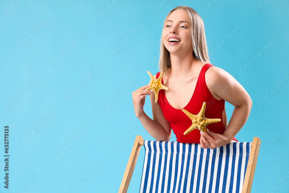 Beautiful young woman with starfishes and deck chair on blue background