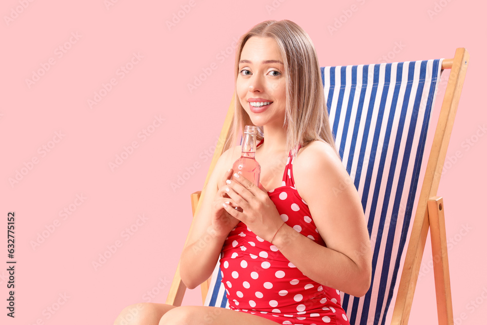 Beautiful young woman with soda relaxing in deck chair on pink background