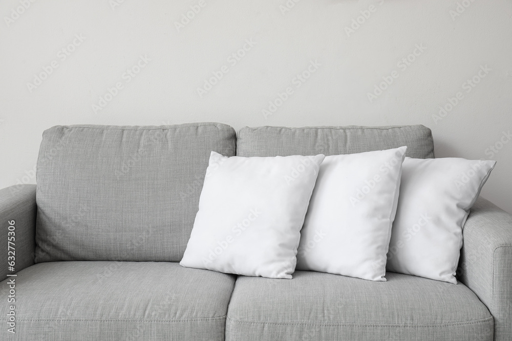 Grey sofa with pillows near white wall