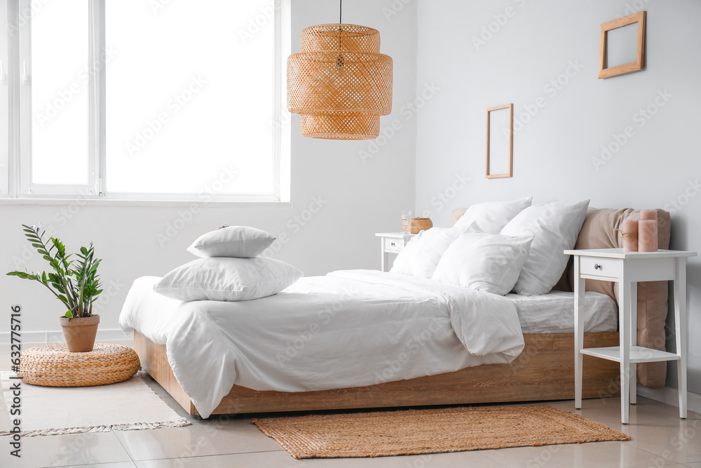 Interior of modern bedroom with comfortable double bed, white pillows, houseplant and wicker lamp