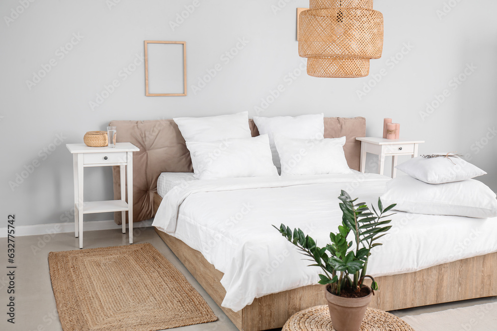 Interior of modern bedroom with comfortable double bed, white pillows, houseplant and wicker lamp