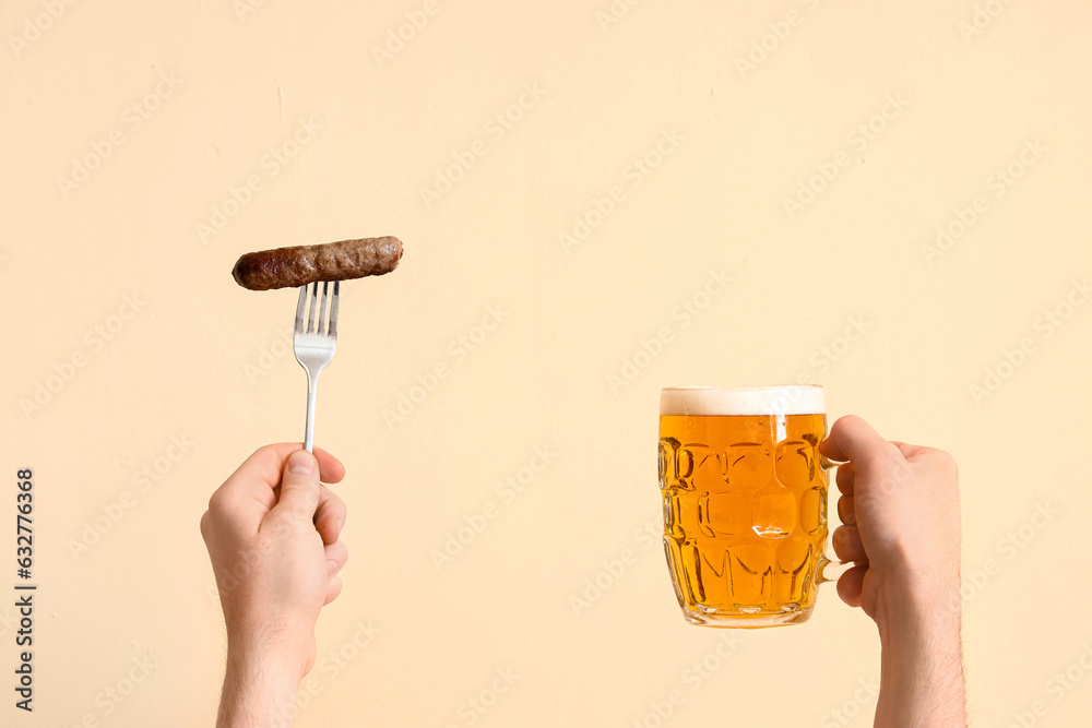 Man with glass of beer and sausage on beige background