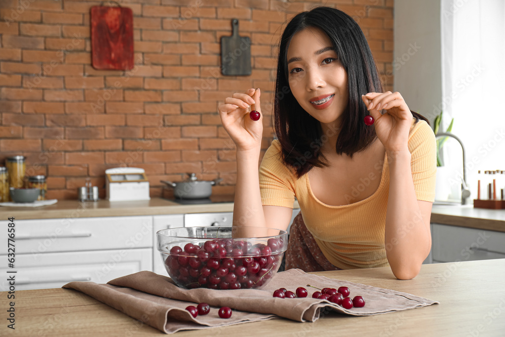 Happy beautiful young Asian woman with bowl of ripe cherries in kitchen