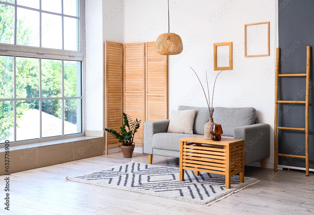 Interior of light living room with grey sofa and branches in vase on wooden table