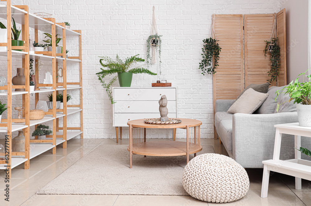 Interior of light living room with grey sofa, wooden coffee table and houseplants