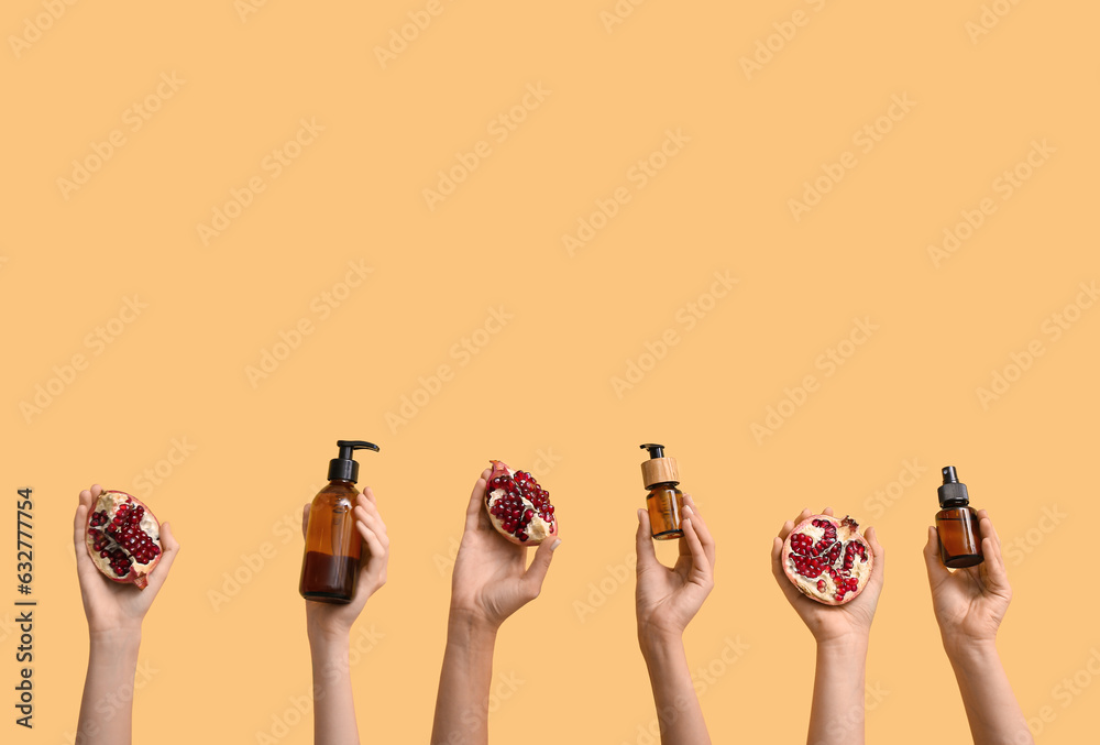 Female hands holding cosmetic products and pomegranate on yellow background