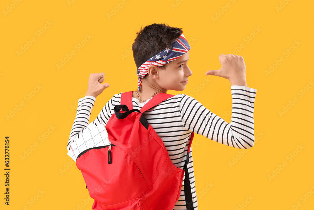 Fashionable schoolboy pointing at red backpack on orange background