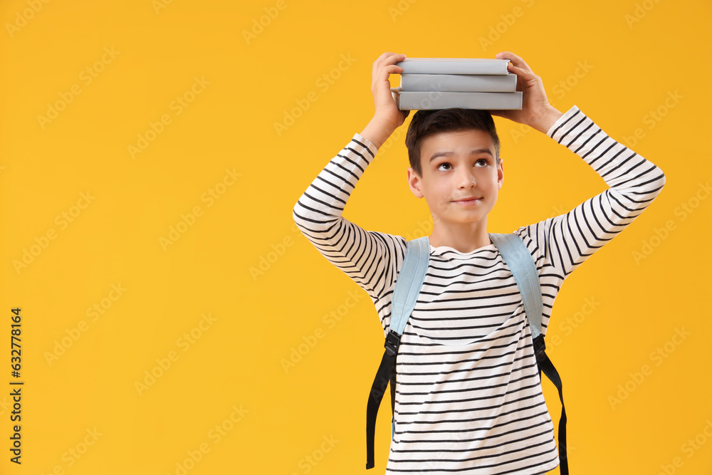 Portrait of schoolboy with backpack holding books on his head against orange background