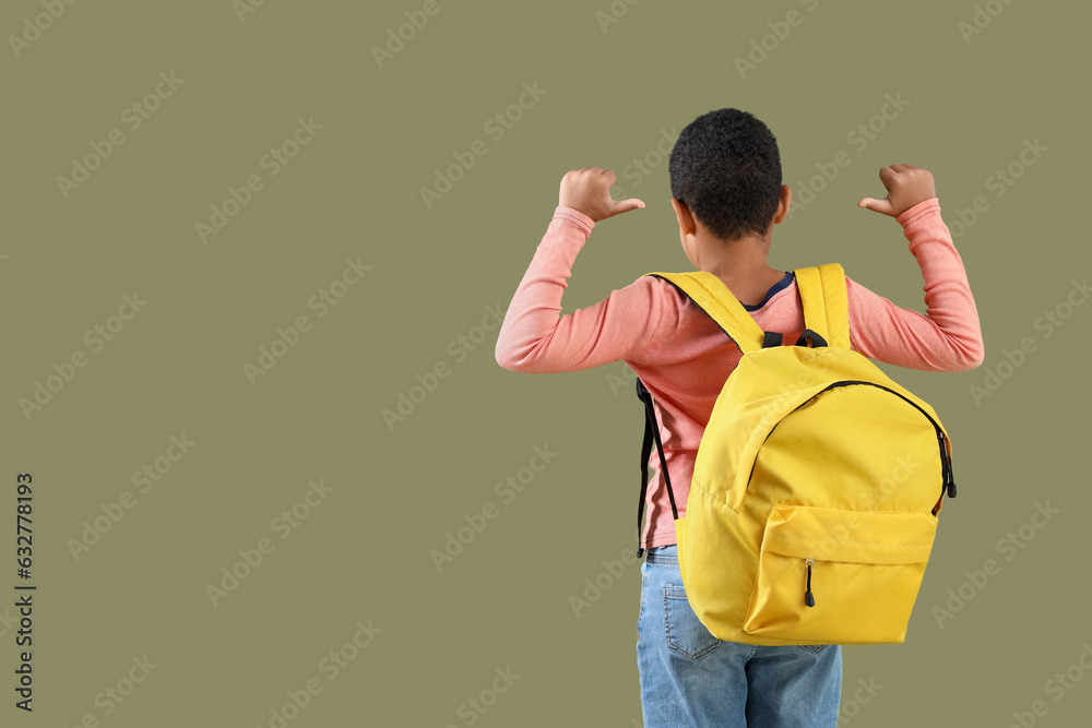 Little African-American boy pointing at school backpack on green background, back view