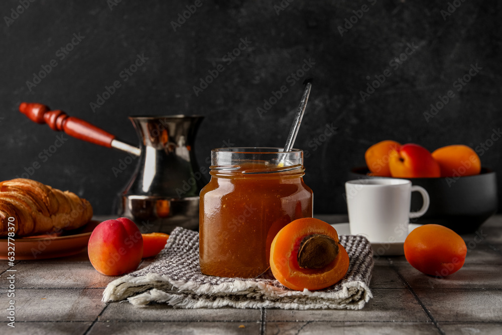 Jar with sweet apricot jam and cup of coffee on grey tile table