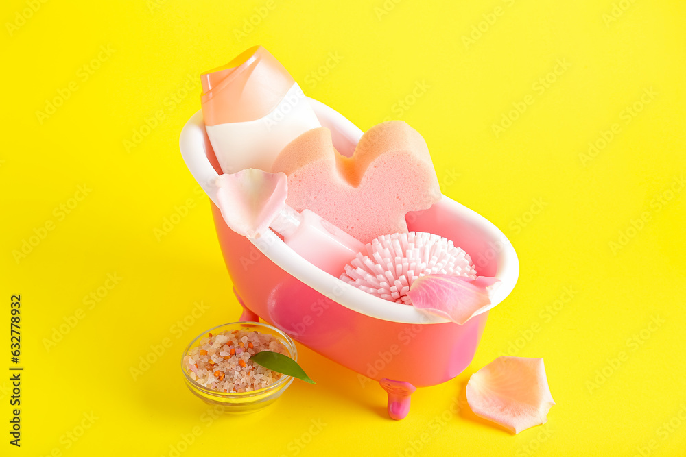 Small bathtub with bath supplies on yellow background