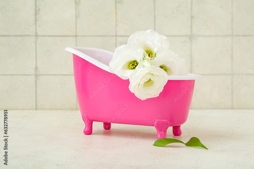 Small bathtub and beautiful eustoma flowers on light table