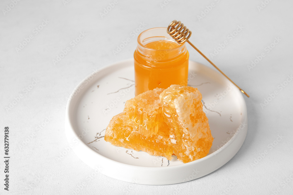 Plate with jar of honey, dipper and combs on light background