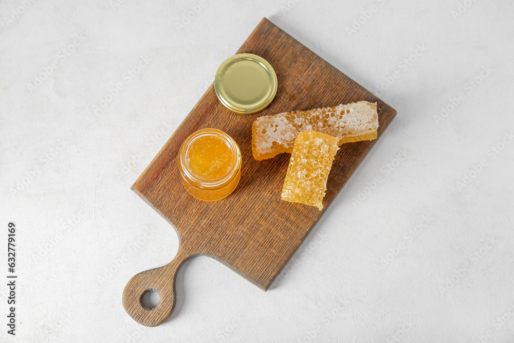 Wooden board with jar of tasty honey and combs on light background