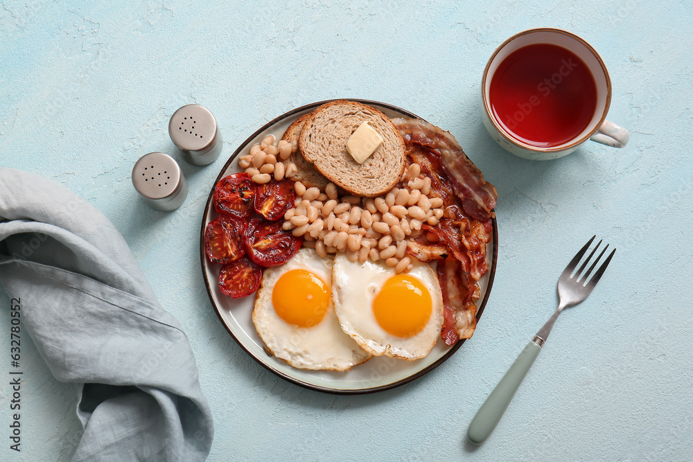 Plate with tasty English breakfast and cup of tea on blue background