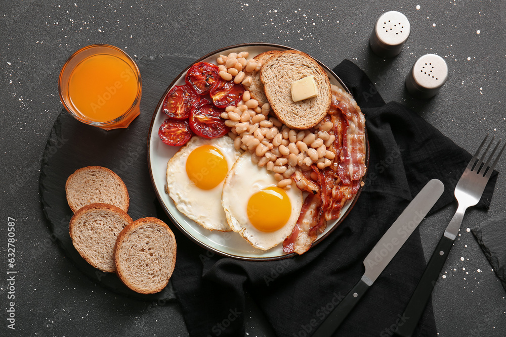 Plate with tasty English breakfast and glass of juice on black background