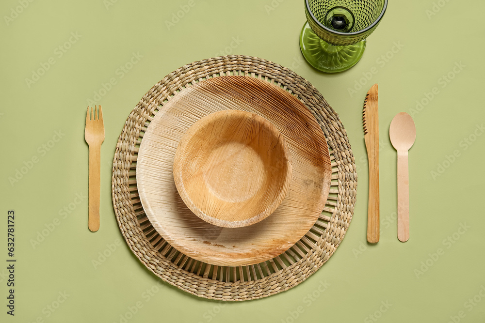 Different wooden tableware and glass on green background