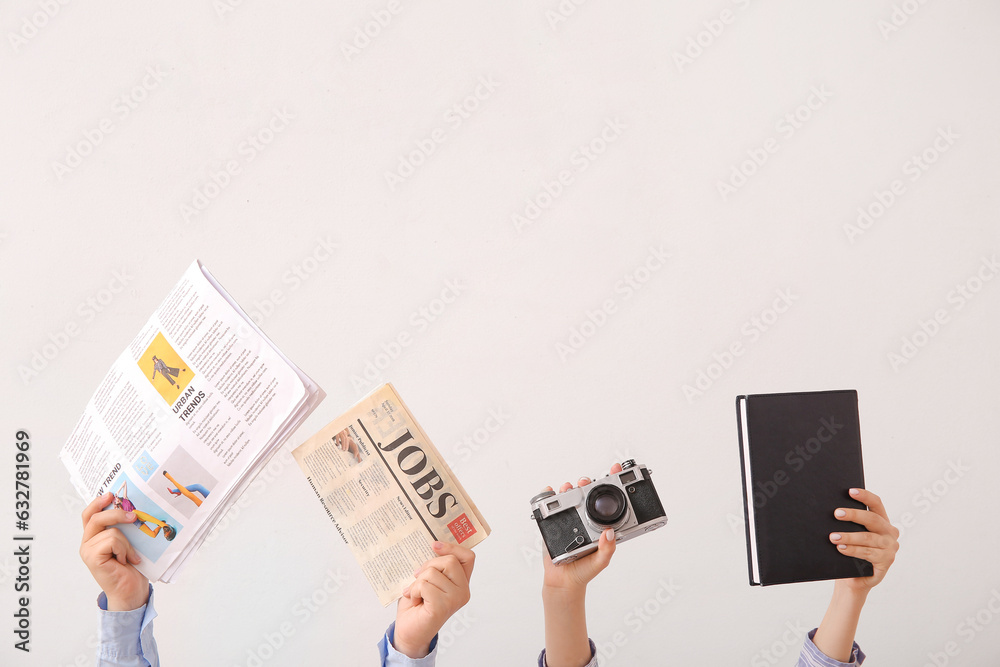 Female hands with newspapers, photo camera and notebook on light background