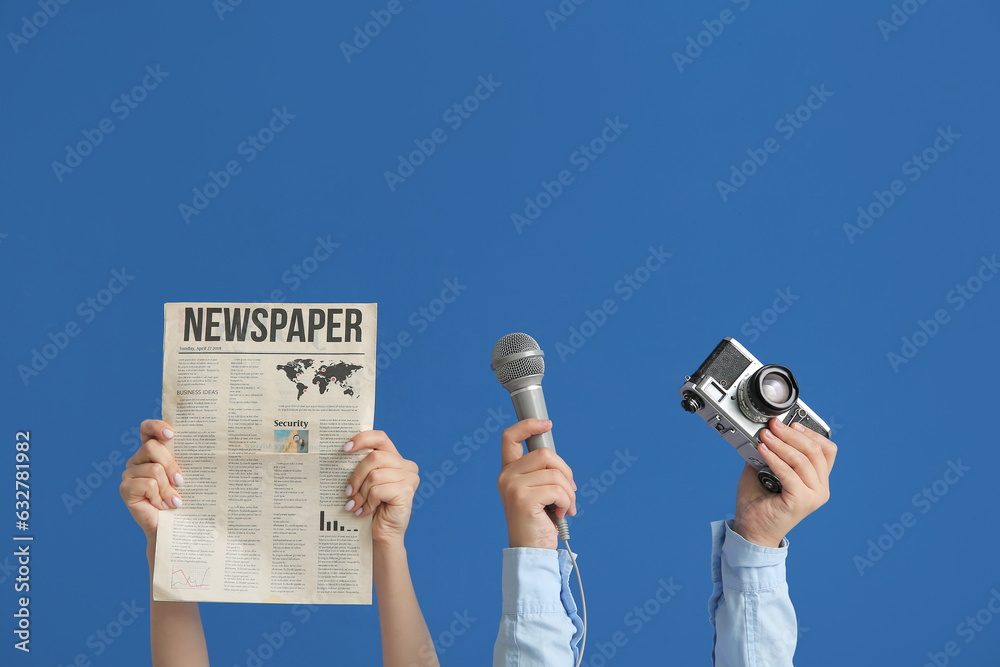 Female hands with newspaper, microphone and photo camera on blue background