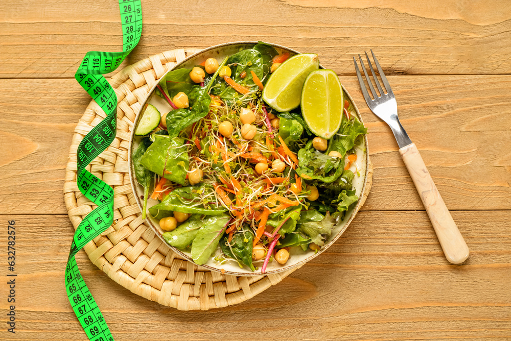 Plate with fresh salad and measure tape on wooden background. Diet concept