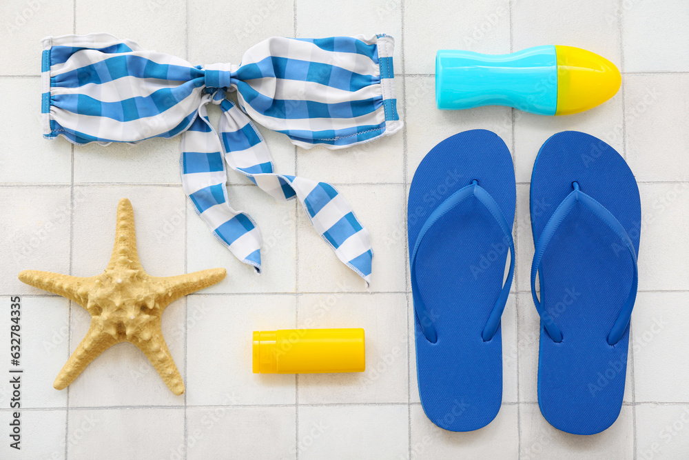 Pair of blue flip flops with swimsuit and sunscreen cream on white tile background