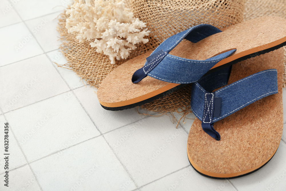 Pair of flip flops with straw hat and coral on white tile background