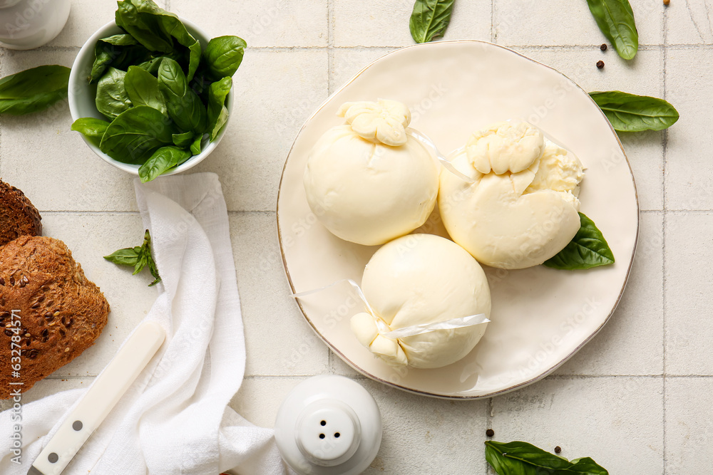 Plate of tasty Burrata cheese with basil on white tile background