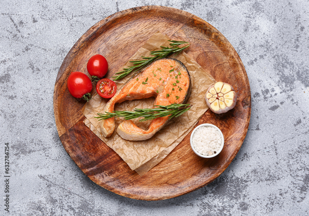 Plate of tasty salmon steak with tomatoes and garlic on grey background